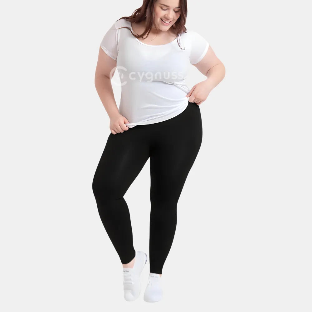 Mulher plus size sorridente usando a Legging Jade Fit moldeador de Cós Alto na color preta, combinada con camiseta branca y tênis, em pose descontraída que evidencia a versatilidade y comodidad da peça para o dia a dia.