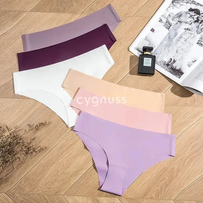 Imagem de calzones sin costuras da Cygnuss dispostas em um fundo de madeira, apresentando color suaves y elegantes, incluindo lilás, roxo, blanco, rosado y beige. Ao lado, um perfume y uma revista complementam a composição sofisticada.