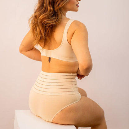 Imagem de mulher usando a calzón moldeador Model - Seca Barriga, vista de espalda. A peça de alta compresión é de tom beige, con listras horizontais na faixa superior, proporcionando controle da barriga y moldeado eficiente da silhueta.