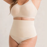 Mulher vestindo a calzón moldeador Pêra da Cygnuss, modelo tanga na color beige, con cintura alta canelada y tejidos ajustado ao corpo, combinando con top sin relleno no mesmo tom.