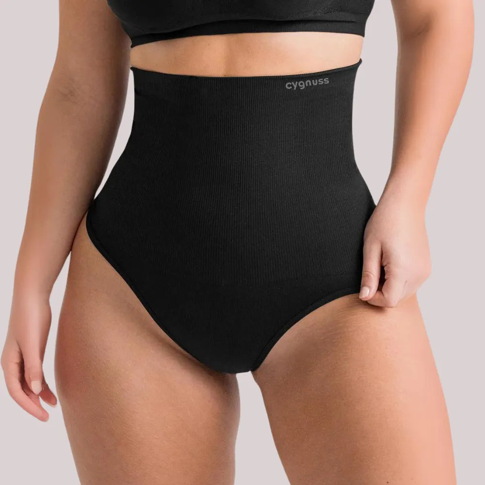 Mulher vestindo a calzón moldeador Pêra da Cygnuss, modelo tanga na color preta, con cintura super alta y tejidos compressivo, destacando a moldeado do abdômen y o caimento firme no corpo.