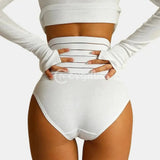 Imagem de uma mulher de espalda, usando uma faja moldeadora branca con faixas de compresión horizontais. A mulher também está vestindo um top de manga longa blanco, con as mãos na cintura, destacando a forma da silhueta modelada pela cinta.
