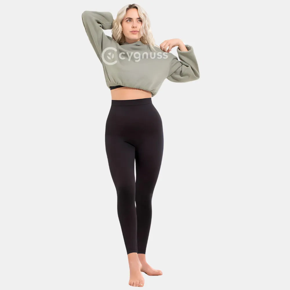 Mulher sorrindo, usando a Legging Jade Fit moldeador de Cós Alto na color preta, combinada con hoodie verde, em pose descontraída que destaca o cós alto y o caimento cómodo da peça.