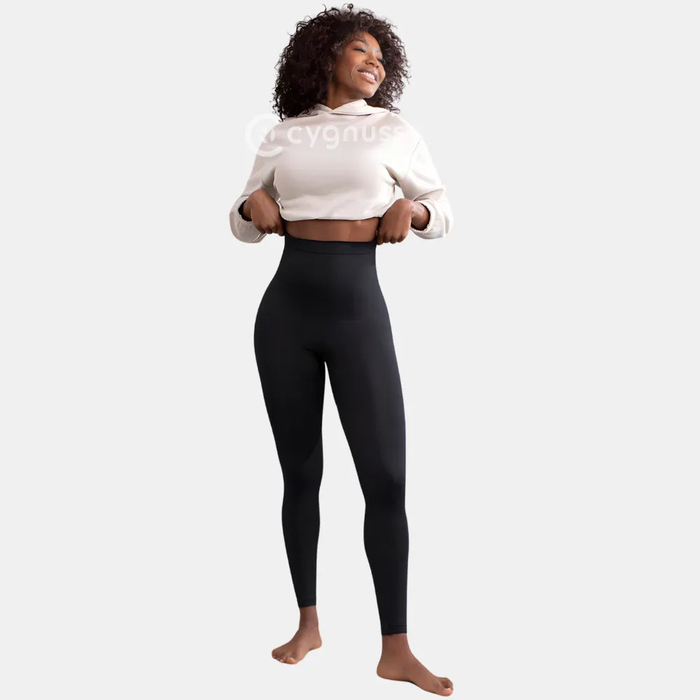 Mulher sorridente usando a Legging Jade Fit moldeador de Cós Alto na color preta, combinada con moletom cropped beige, em pose leve y descontraída que destaca o cós alto y o ajuste anatômico da peça.