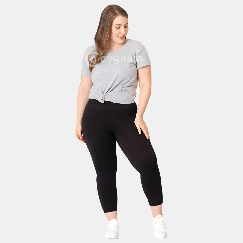 Mulher plus size usando a Legging Jade Fit moldeador de Cós Alto na color preta, combinada con camiseta gris amarrada y tênis blanco, em pose descontraída que evidencia o comodidad y a versatilidade da peça no dia a dia.
