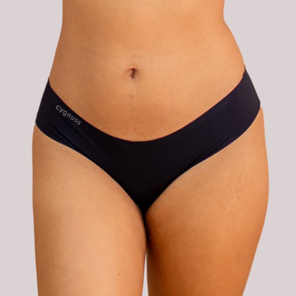 magem frontal da região do quadril de uma mulher usando uma calzón preta fio-dental sin costuras da Cygnuss. O design ajusta-se ao corpo con comodidad y discrição.
