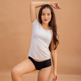 Mulher posando con uma camiseta branca y calzón preta sin costuras da Cygnuss. con um fundo em tom terroso, a imagem destaca o ajuste cómodo y a elegância discreta da peça.