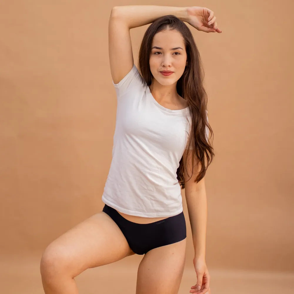 Mulher posando con uma camiseta branca y calzón preta sin costuras da Cygnuss. con um fundo em tom terroso, a imagem destaca o ajuste cómodo y a elegância discreta da peça.