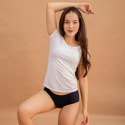 Mulher posando con uma camiseta branca y calzón preta sin costuras da Cygnuss. con um fundo em tom terroso, a imagem destaca o ajuste cómodo y a elegância discreta da peça.