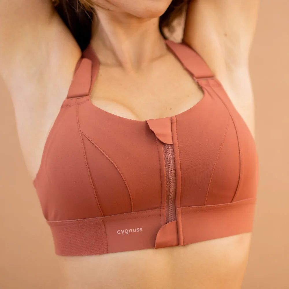 Detalhe do sostén esportivo Cygnuss na color terracota, evidenciando o cierre frontal con zíper y aba protetora para maior comodidad y praticidade no uso